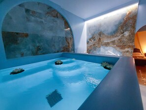 Une salle de spa moderne dotée d’une grande baignoire, d’un plafond en arc de cercle et de murs en marbre.