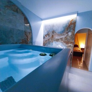 Un baño moderno con una bañera grande, una pared de piedra y una pequeña zona de estar.