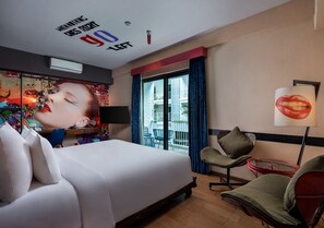 A hotel room with a bed, a chair, a table, and a window with curtains.