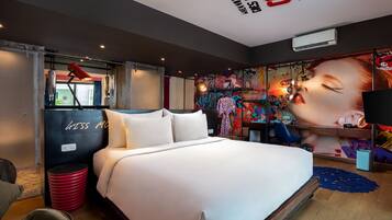 Una camera d'albergo moderna con un letto grande, un cestino della spazzatura rosso e una parete decorata con opere d'arte colorate.