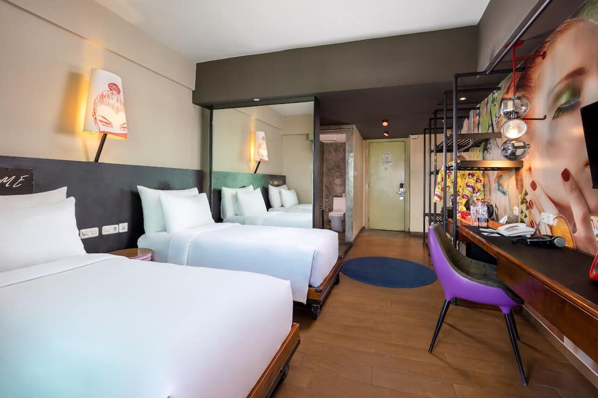A hotel room with two beds, a desk, and a bathroom visible through an open door.