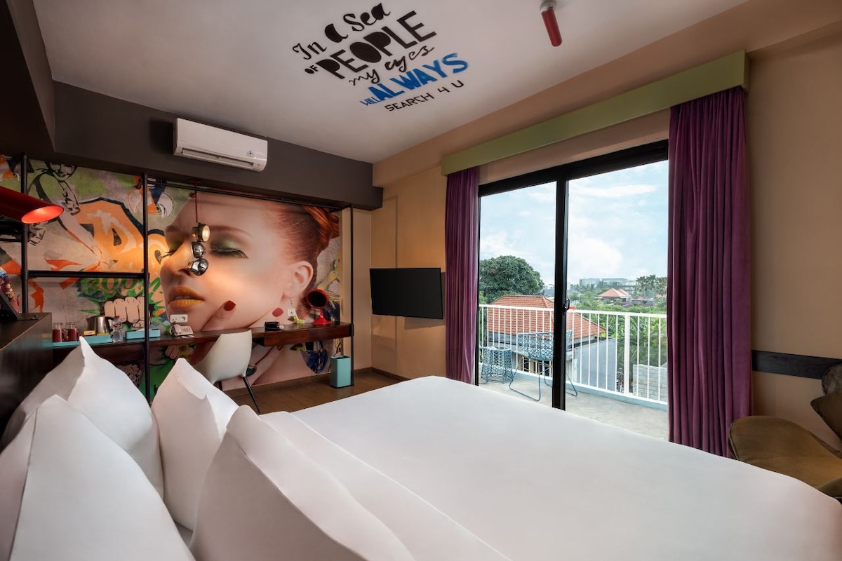 A hotel room with a large bed, a view of the city, and a mural on the wall.