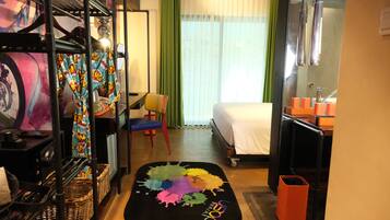 Habitación de hotel con cama, escritorio, silla, alfombra colorida y ventana con cortinas.