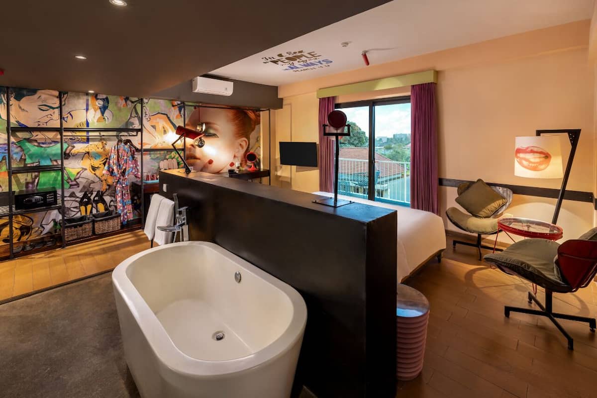 A modern hotel room with a large bathtub, a bed, a TV, and a balcony with a city view.