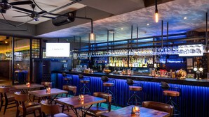 A bar with wooden tables and stools, a counter with bottles, and a screen displaying "C'est la VIE". - Viva Dash Hotel Seminyak (Keroboken Kelod)
