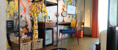 A room with a colorful abstract mural, a desk with a computer, a chair, and a small table with a lamp.