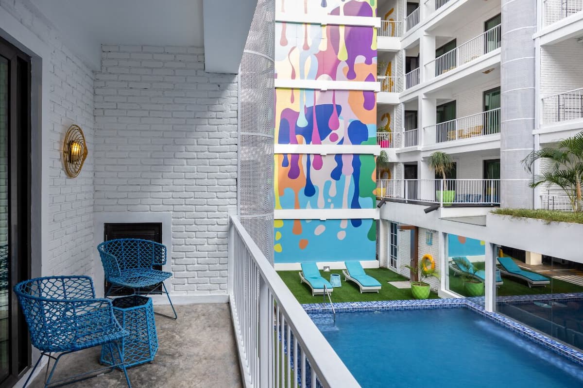 A hotel balcony with a pool, blue chairs, and a colorful wall.