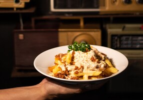 A bowl of pasta with meat sauce and melted cheese, held by a person.