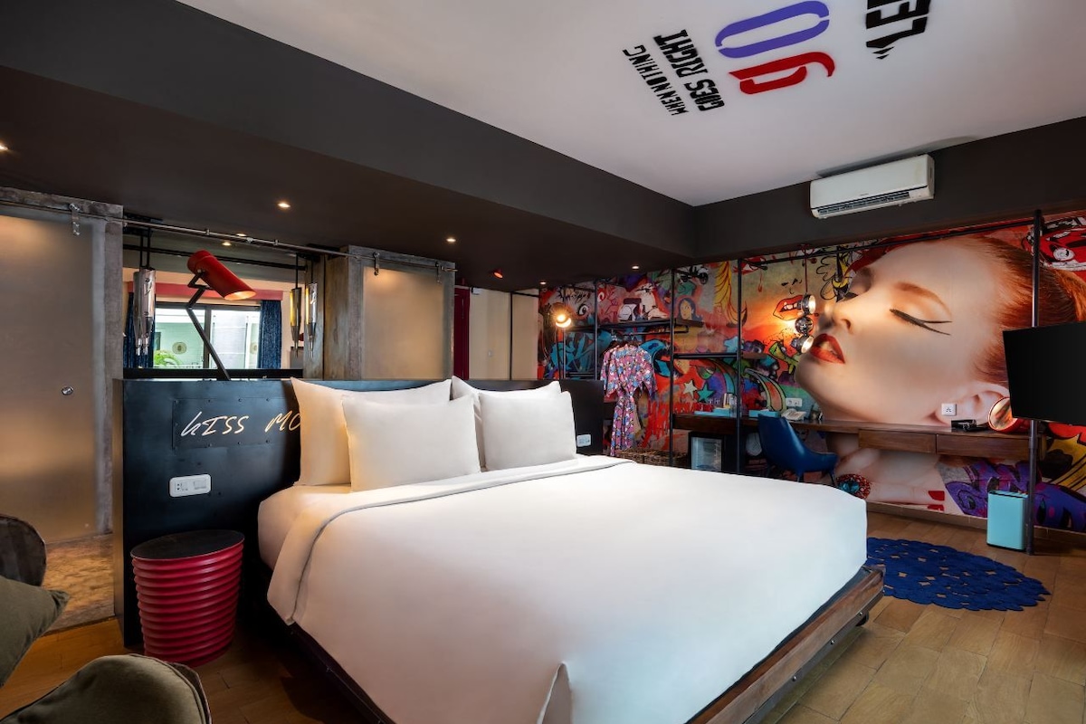 A modern hotel room with a large bed, a desk, and a colorful mural on the wall.