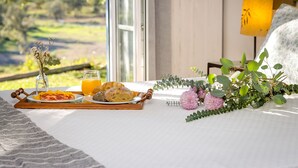 Desayuno listo con una bandeja de comida, un vaso de zumo de naranja y una lámpara sobre la cama, con vistas a la vegetación.