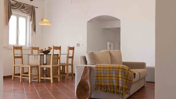 A living room with a sofa, wooden chairs, a dining table, and a large window.