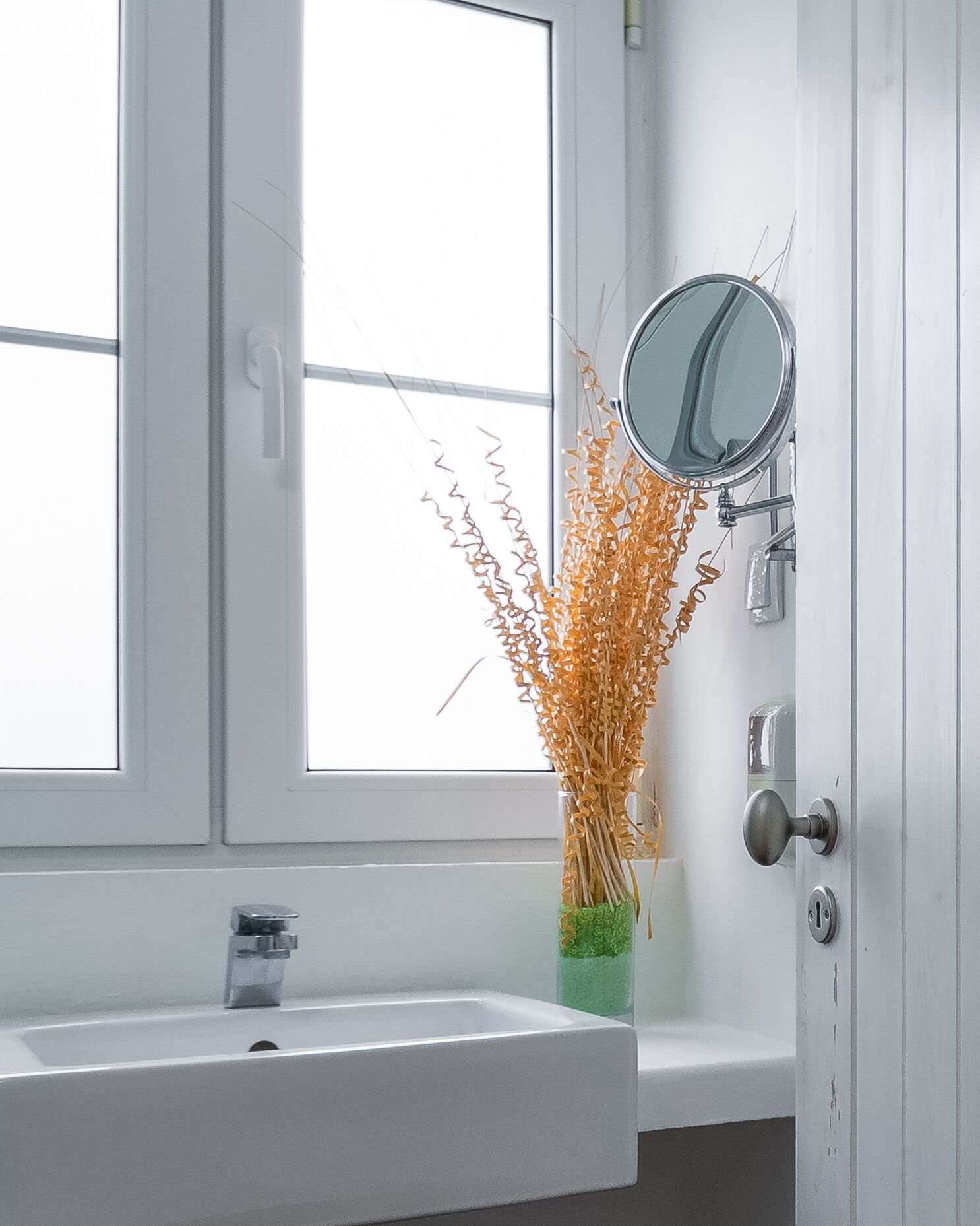 Un baño con lavamanos blanco, espejo y ventana con vistas.
