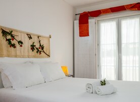Una cama impecablemente tendida con sábanas blancas, un paño decorativo rojo en la ventana y una rama con bayas rojas montada en la pared.