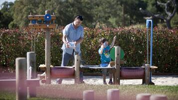 Un parque infantil con un balancín, un lanzador de pelotas y un columpio de neumático.
