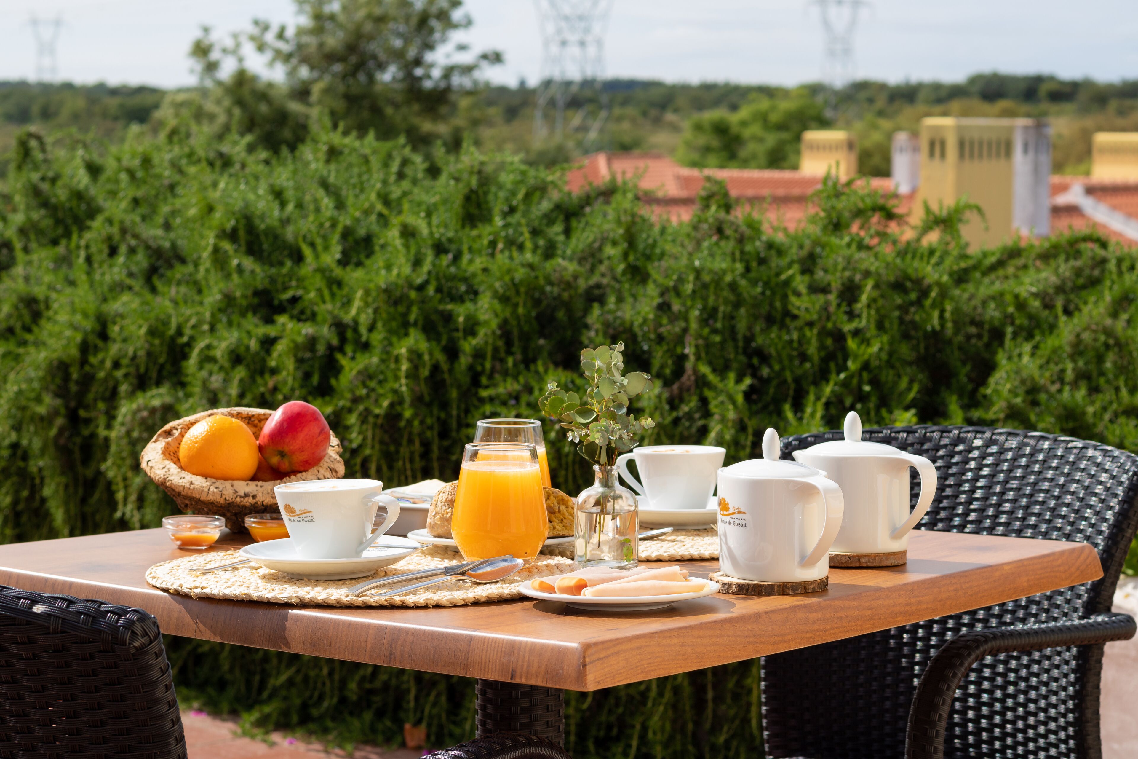 Una mesa de desayuno al aire libre, con vistas a zonas verdes y edificios en el fondo.