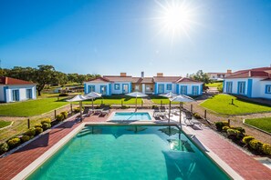 Ein Resort mit einem zentral gelegenen Schwimmbad, mehreren Gästezimmern und einer gepflegten Rasenfläche.