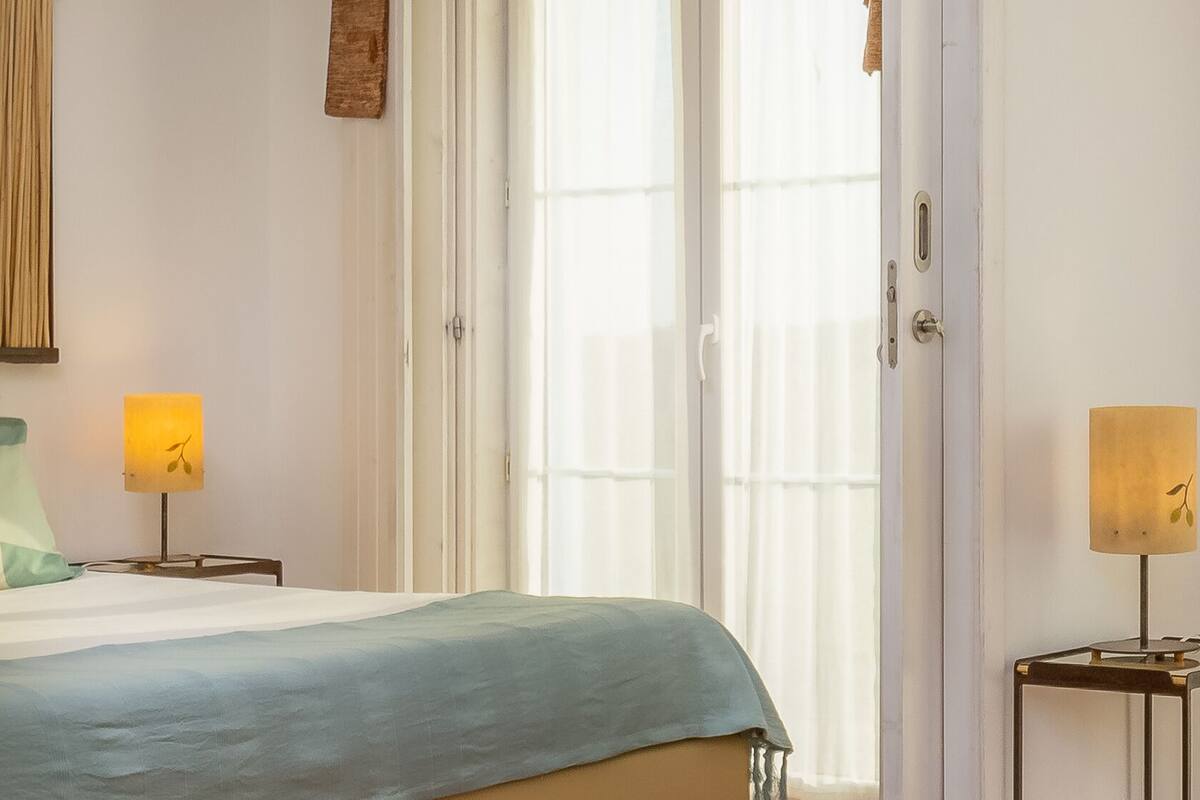 Un dormitorio con una cama, dos lámparas de noche, una ventana con cortinas y una puerta.