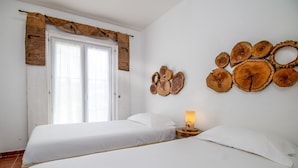 Una habitación con dos camas, una ventana con cortinas y una obra de arte de madera colgada en la pared.