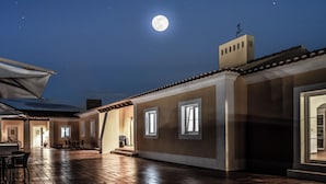 Un patio con suelo de baldosas, una pérgola y un edificio con amplias ventanas.