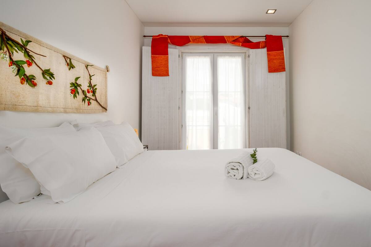 Una cama bien hecha con sábanas blancas, una toalla enrollada y una pequeña planta decorativa.