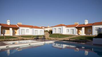 Un área de piscina con una piscina azul cristalina, rodeada de edificios blancos con techos rojos y un cielo despejado.
