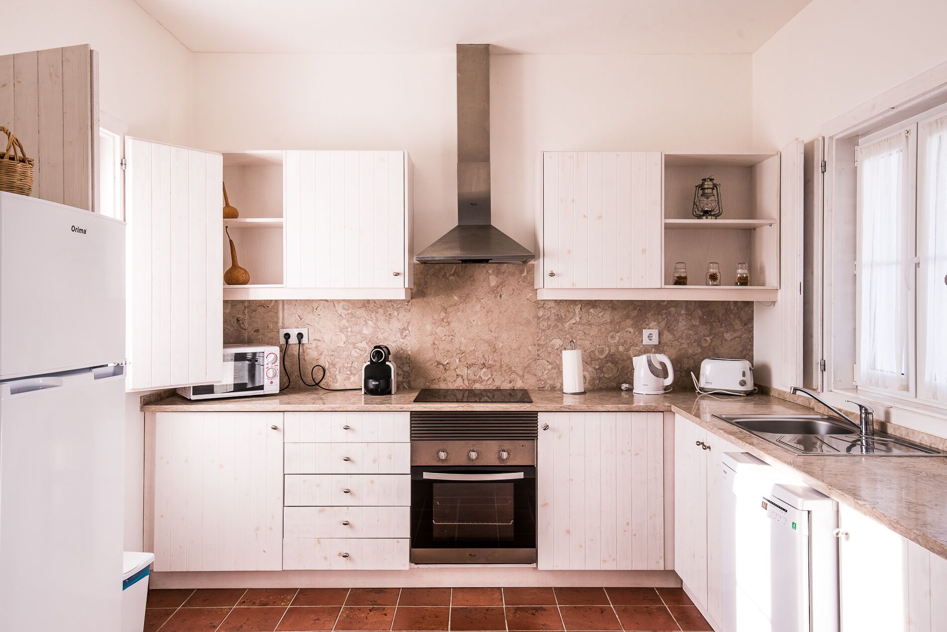 Una cocina moderna con muebles blancos, horno empotrado, microondas y cafetera.