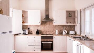 Una cocina moderna con muebles blancos, horno empotrado, microondas y cafetera.