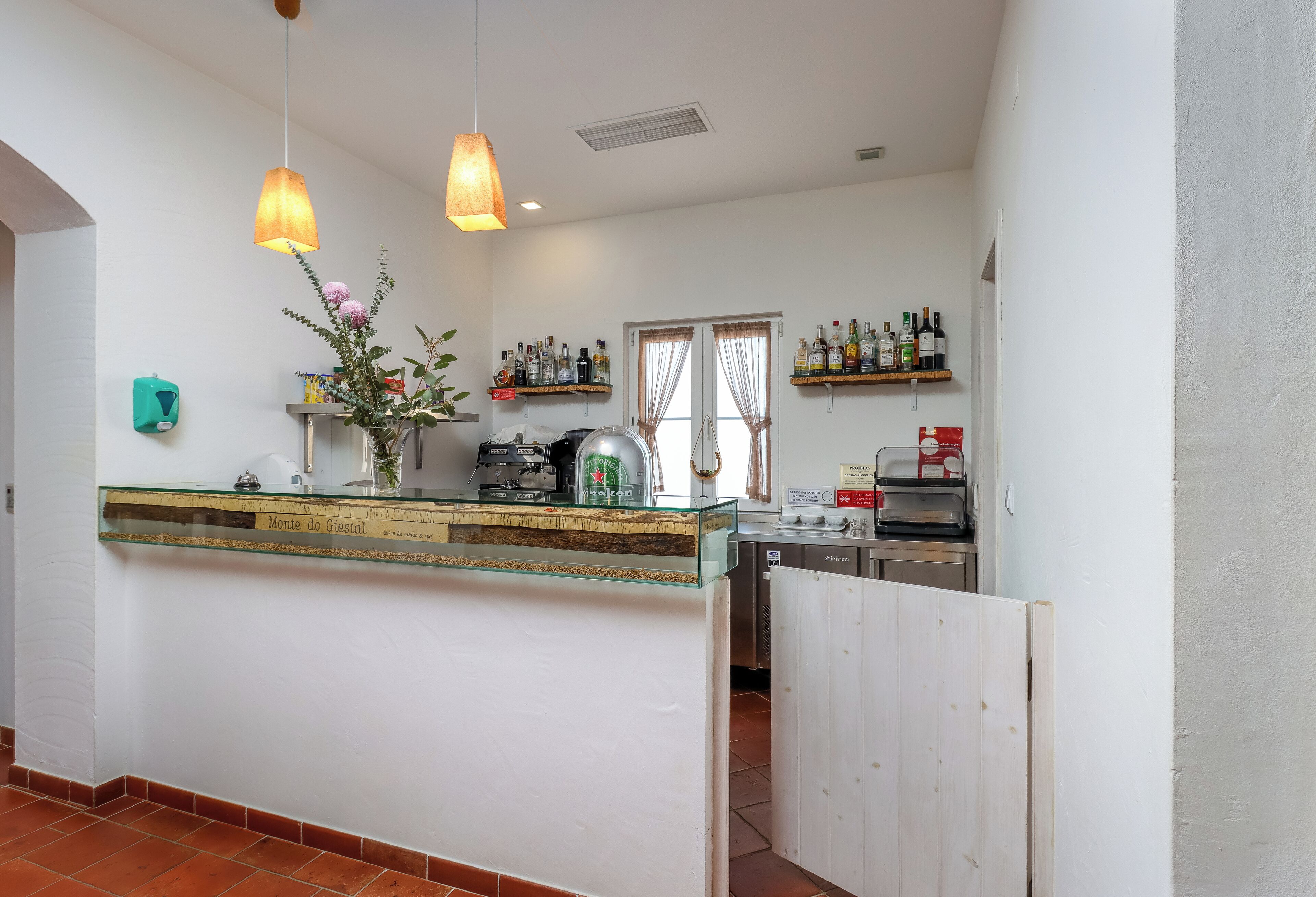 Una cocina con mostrador de vidrio, lámparas colgantes y estantes con botellas.
