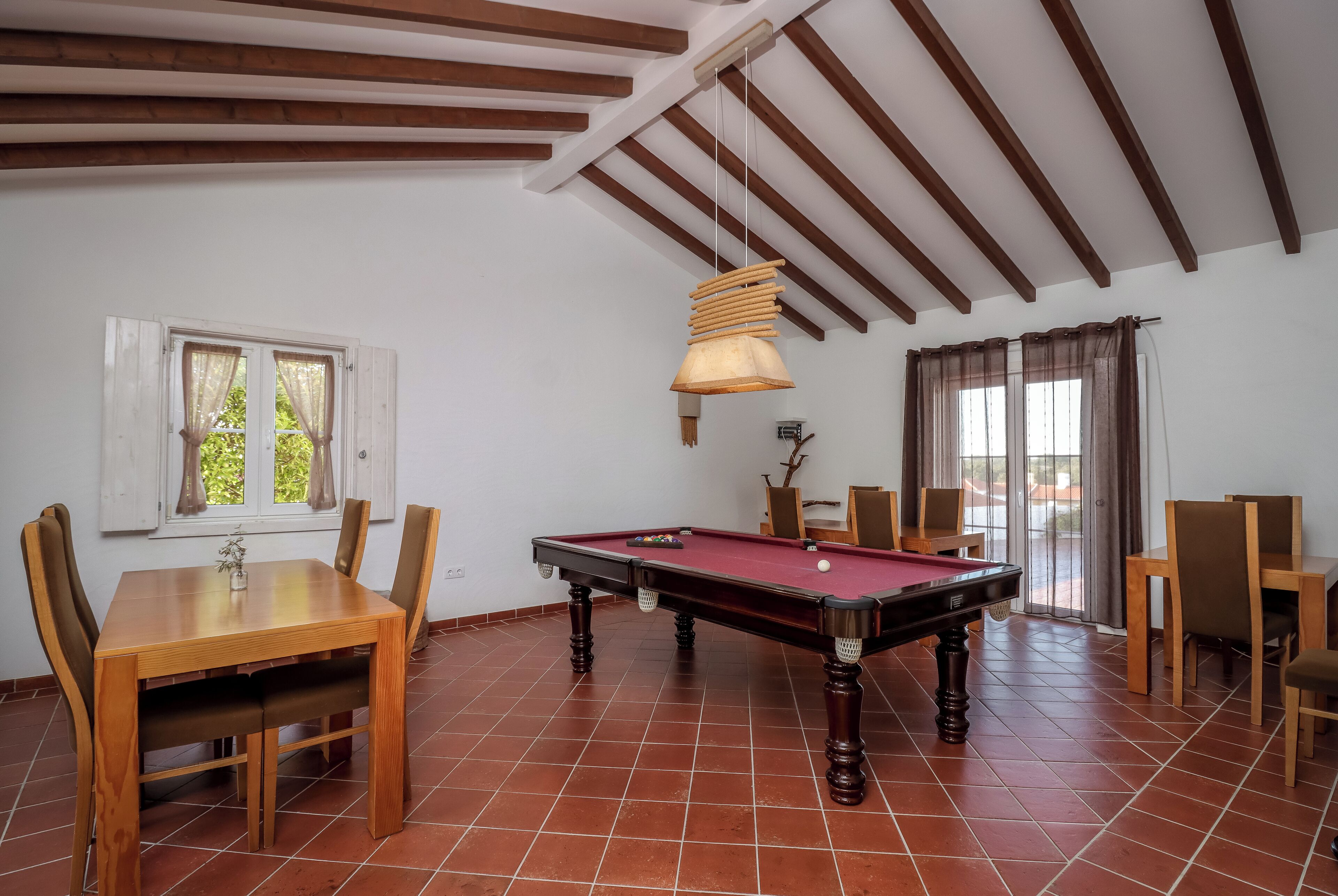 Una habitación con mesa de billar, sillas de madera, mesa de comedor y una lámpara colgante.
