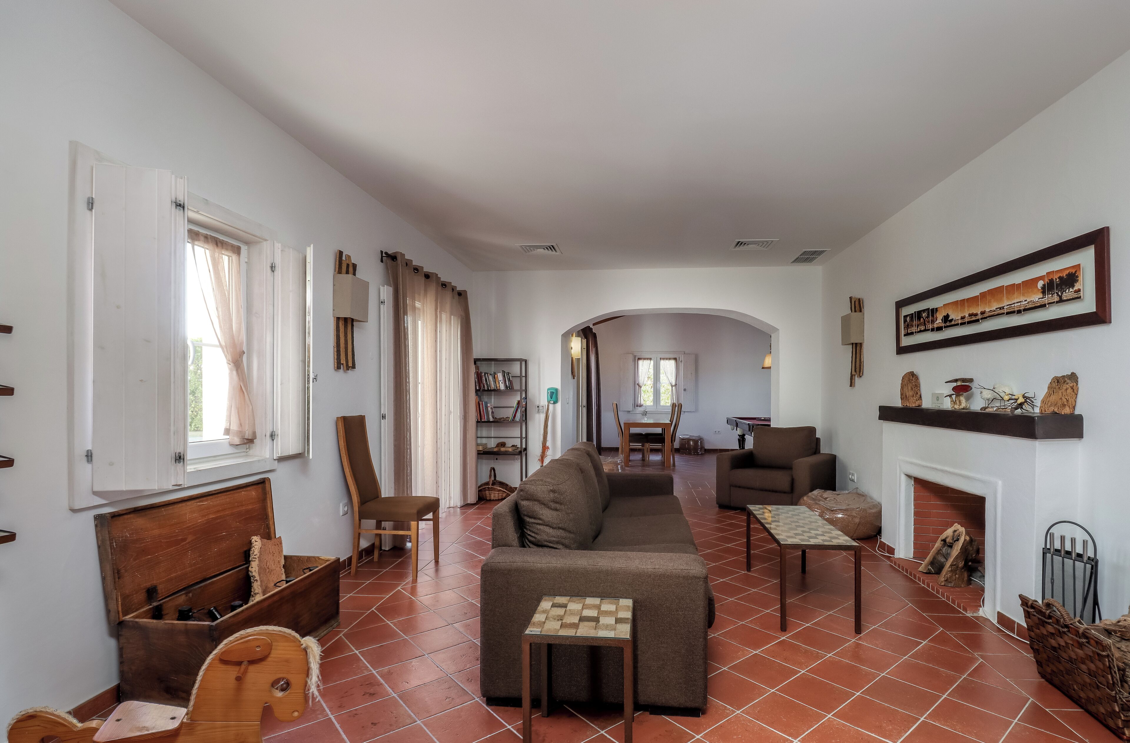 A spacious living room with a sofa, a wooden rocking horse, a chess table, and a fireplace.