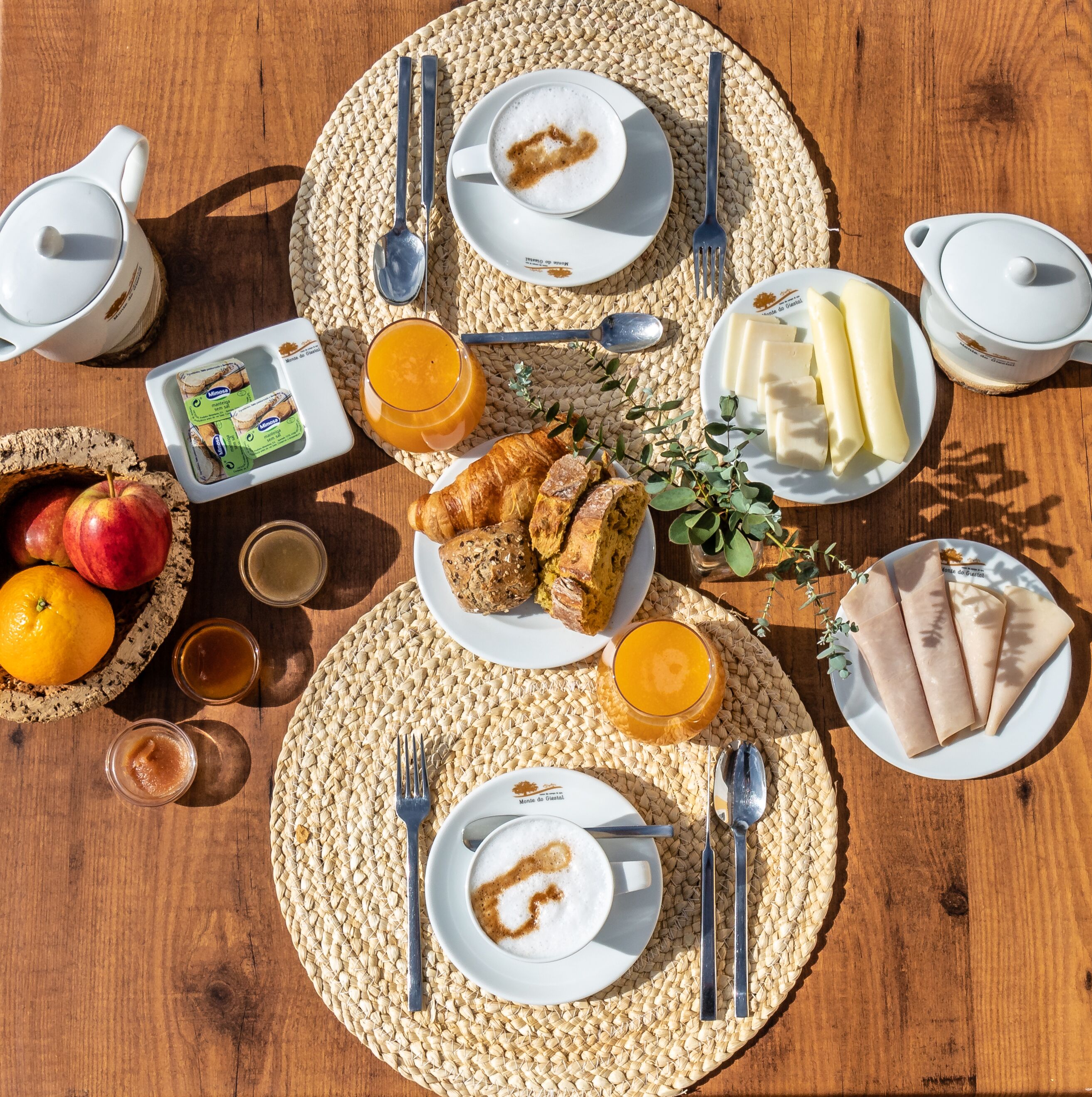 A breakfast setting with a woven placemat, plates of food, a jug of orange juice, and a jug of milk.