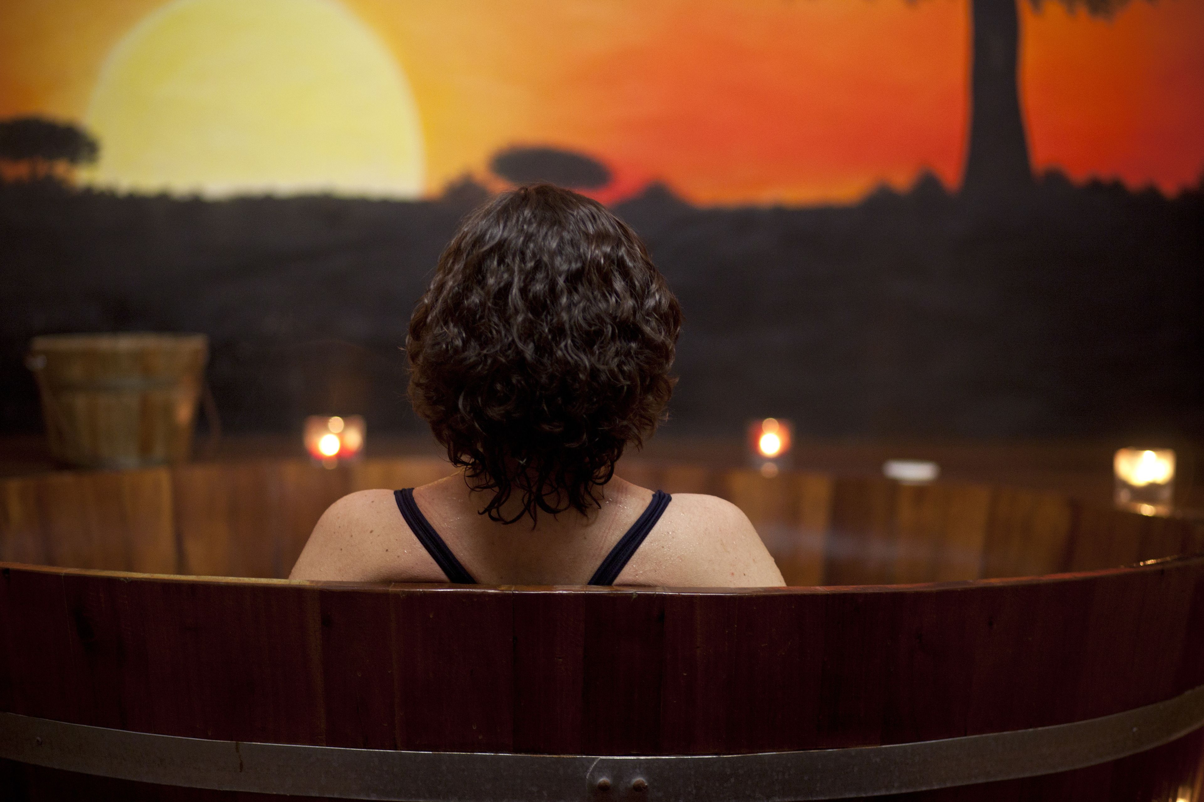 Une personne dans une baignoire en bois, avec un coucher de soleil en arrière-plan.