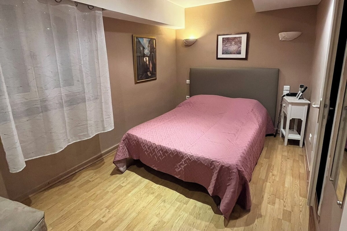 A bedroom with a bed, a nightstand, a wall-mounted lamp, and a door.