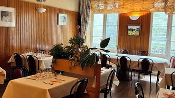 Un comedor con paneles de madera, mesas dispuestas para comer y ventanas amplias con cortinas.