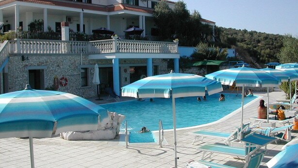A pool area with lounge chairs and umbrellas, a building with a balcony, and a stone wall. - Villaggio Turistico Il Falco (Vieste)