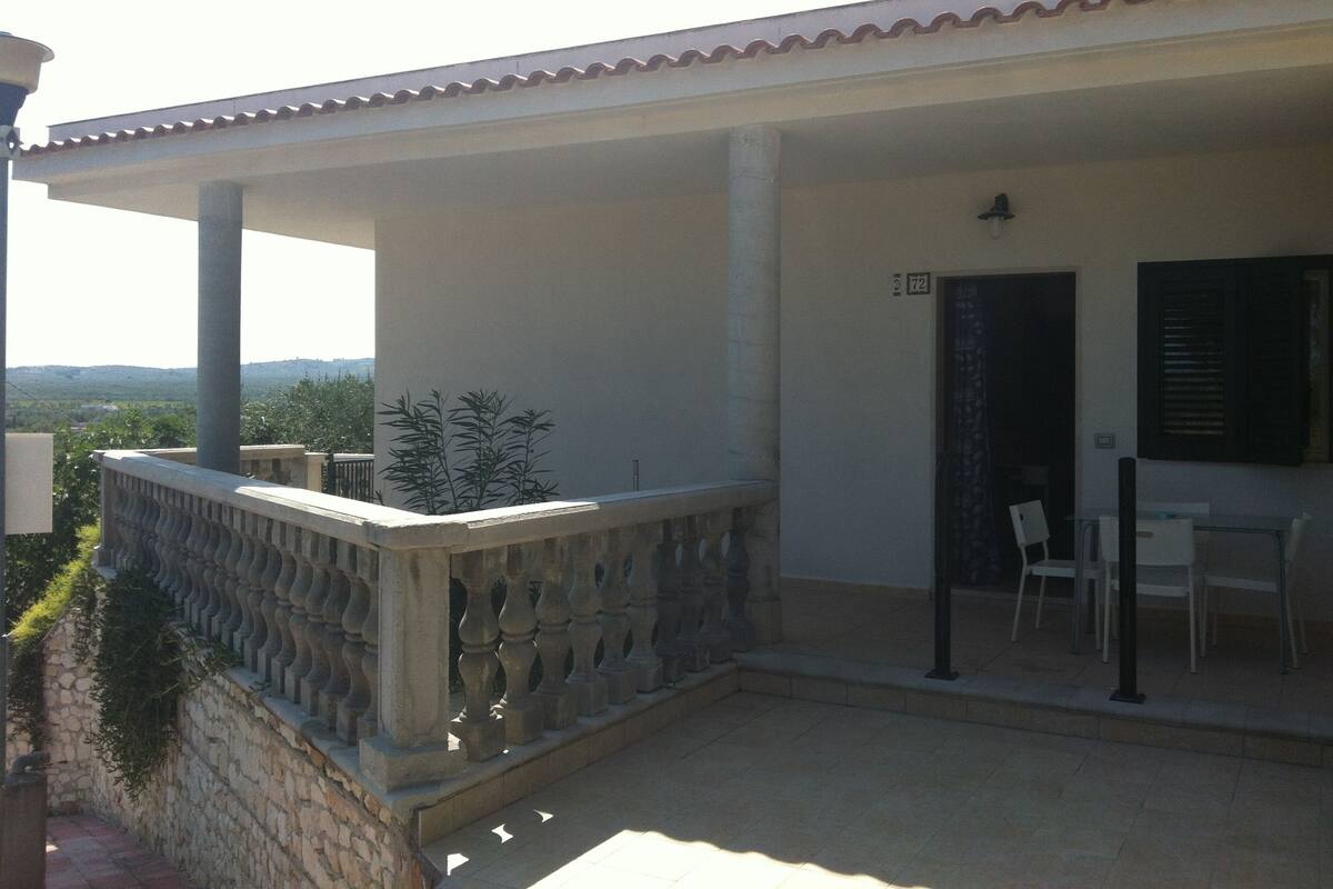 A covered outdoor area with a stone wall, a metal railing, and a table with chairs.