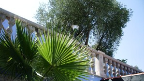 A stone wall with a palm tree in the foreground and a balcony with balusters. - Villaggio Turistico Il Falco (Vieste)