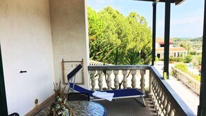 A balcony with a blue chair, a small table with a potted plant, and a view of greenery and buildings in the distance. - Villaggio Turistico Il Falco (Vieste)