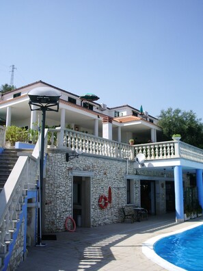 A building with a stone facade, a pool, and a covered outdoor area with a railing.