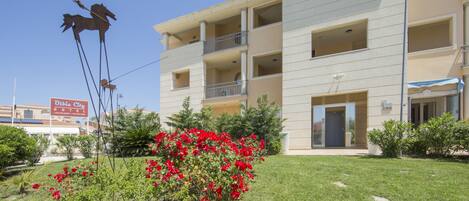 Un hôtel à plusieurs étages doté de balcons, une enseigne indiquant « Olivia City Hotel », et une pelouse bien entretenue agrémentée de fleurs rouges.