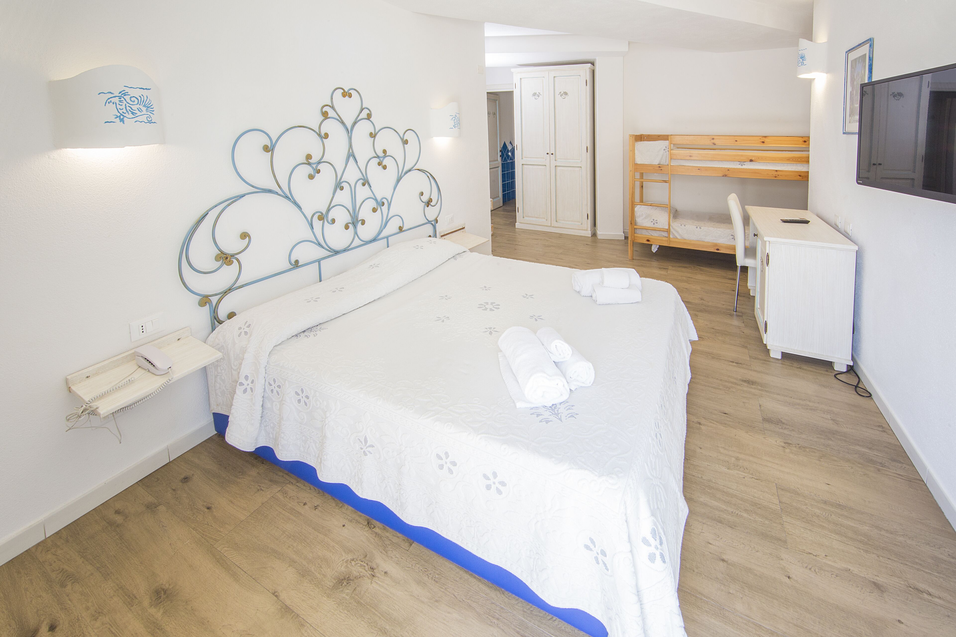 Een slaapkamer met een bed, nachtkastje, lamp, garderobe, bureau, stoel en een televisie.