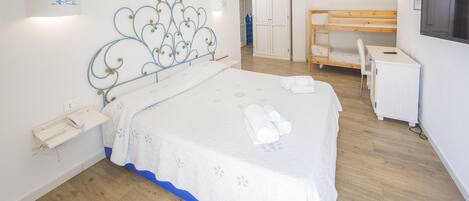 A bedroom with a bed, bedside table, lamp, wardrobe, desk, chair, and a television.