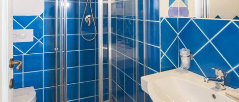 Ein Badezimmer mit einer Duschkabine, einem weißen Waschbecken und blauen Fliesen.