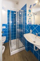 Un baño con ducha de vidrio, lavamanos blanco y paredes con azulejos azules.