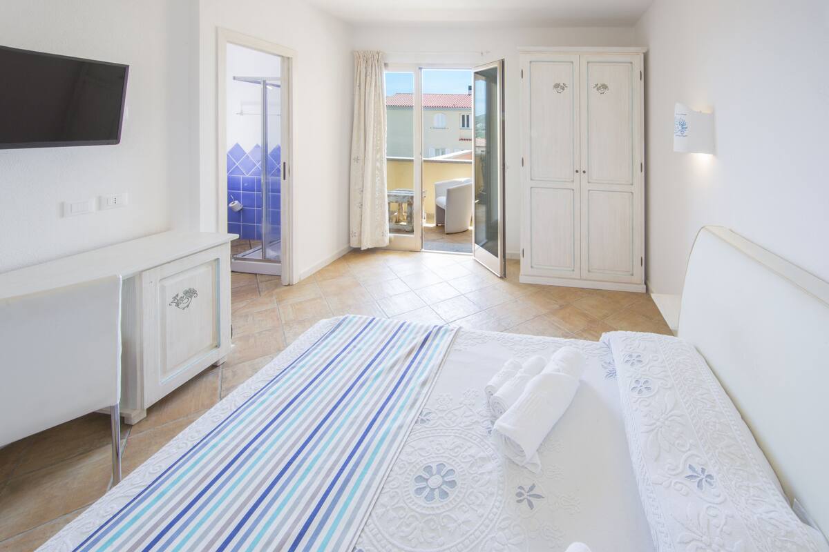 A hotel room with a bed, a TV, a wardrobe, and a bathroom visible through an open door.