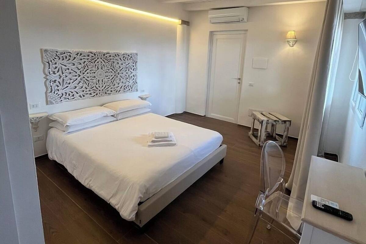 A bedroom with a bed, bedside table, lamp, and a small wooden stool.