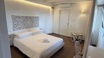 Un dormitorio con cama, mesita de noche, lámpara y un taburete de madera.