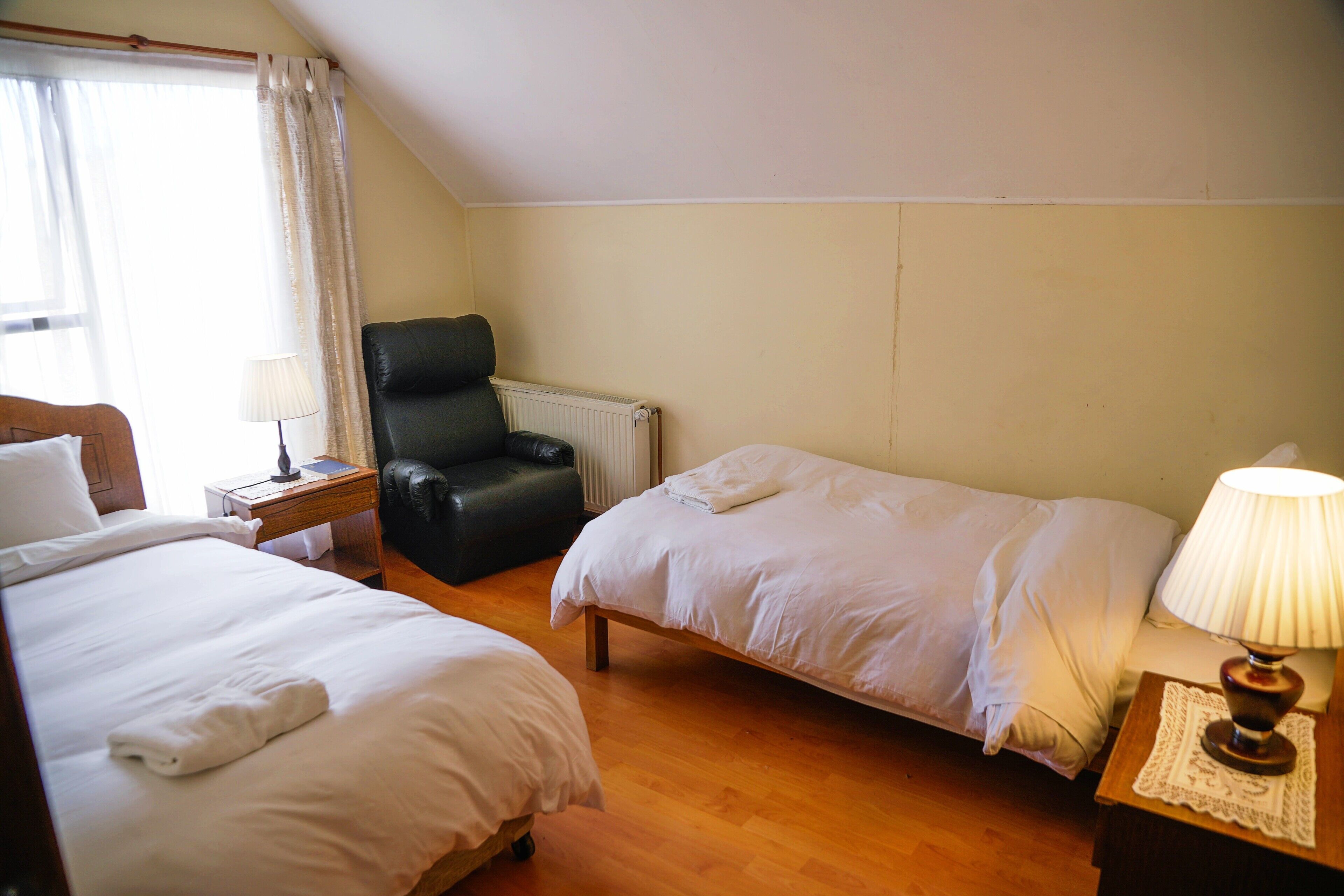 A hotel room with two beds, a chair, a nightstand, and a lamp.