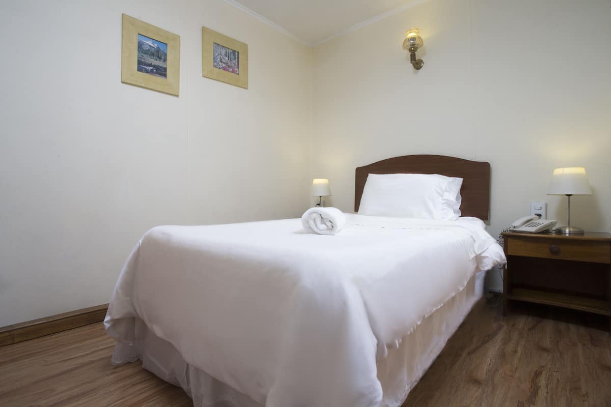 Una cama bien tendida con sábanas blancas, cabecera de madera y dos lámparas de noche.