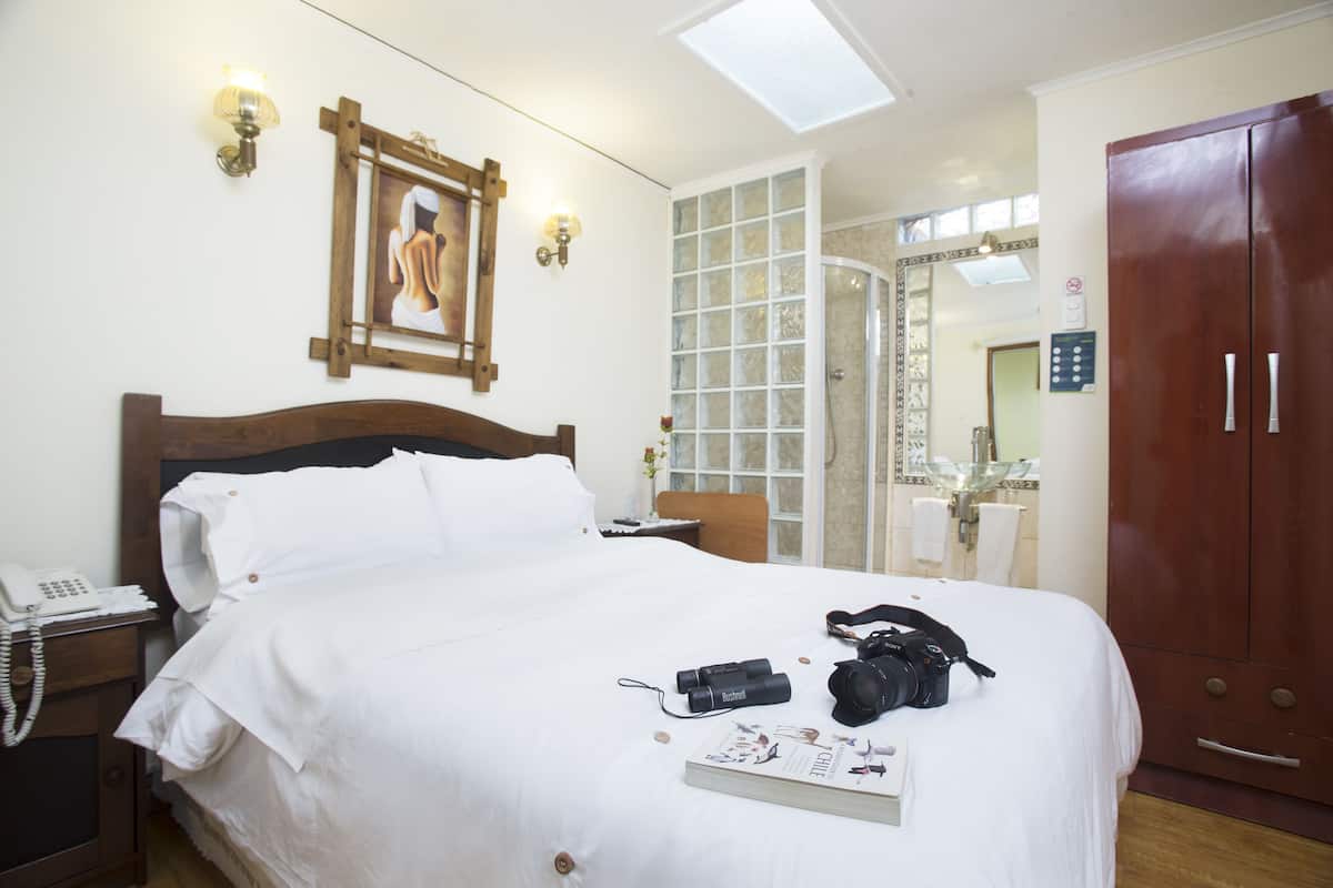 Una habitación de hotel con una cama grande, un teléfono en la mesita de noche, una cámara y un libro sobre la cama.